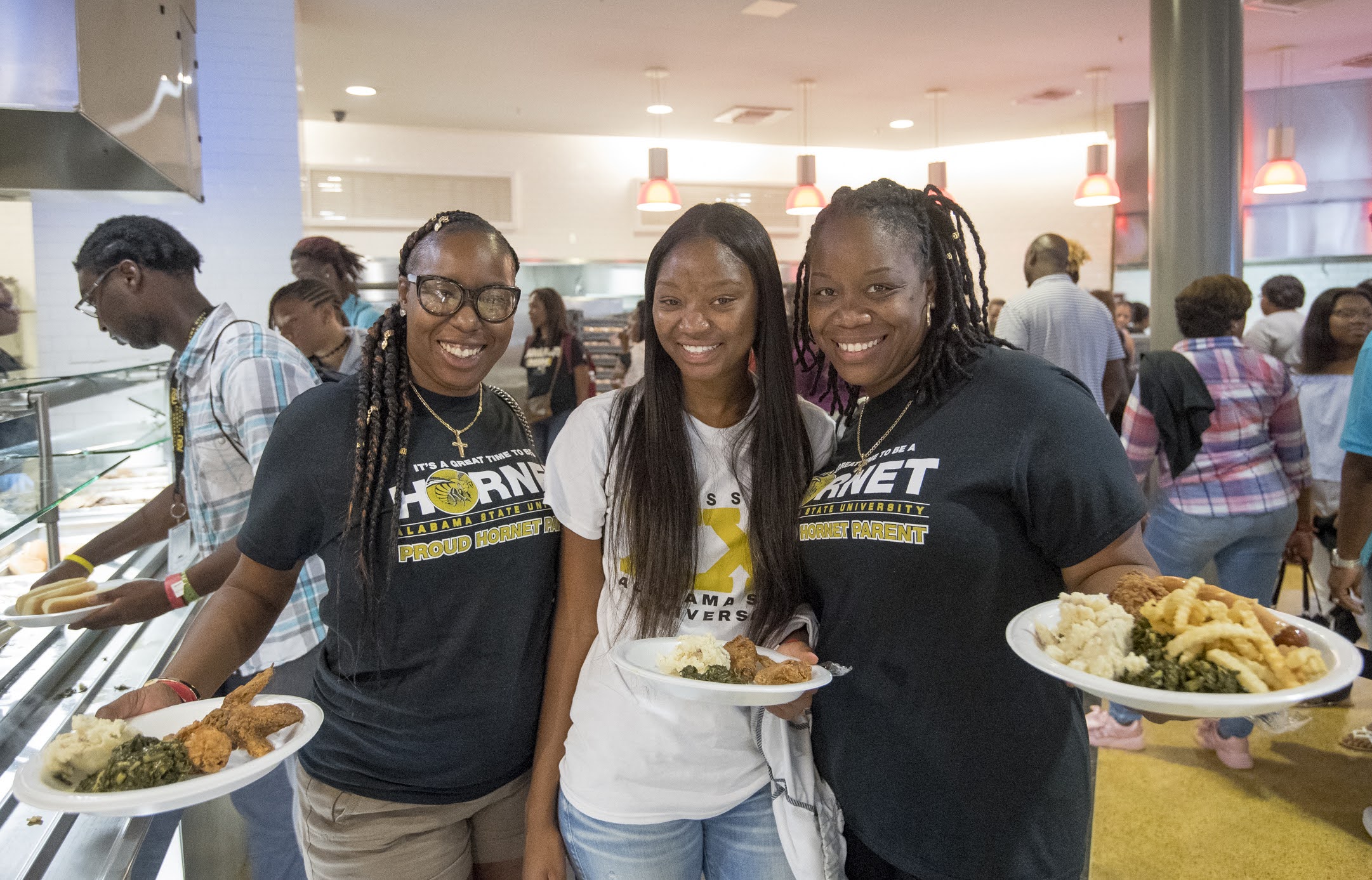 Three people eating at Alabama State, holding a plate of fried chicken, mashed potatoes, and green beans.