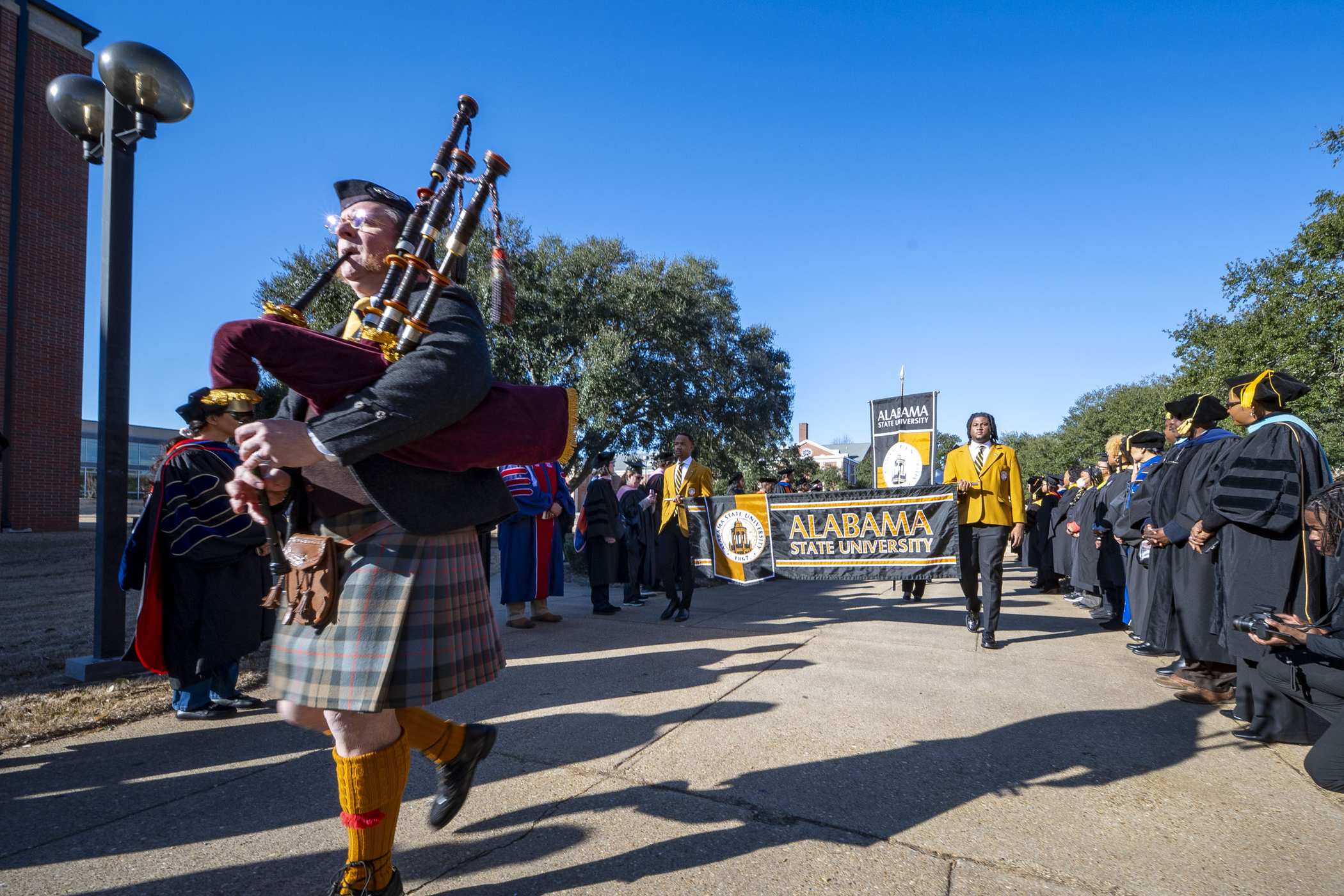 Faculty in academic regalia process behind the Alabama State University banner at a recent commencement.