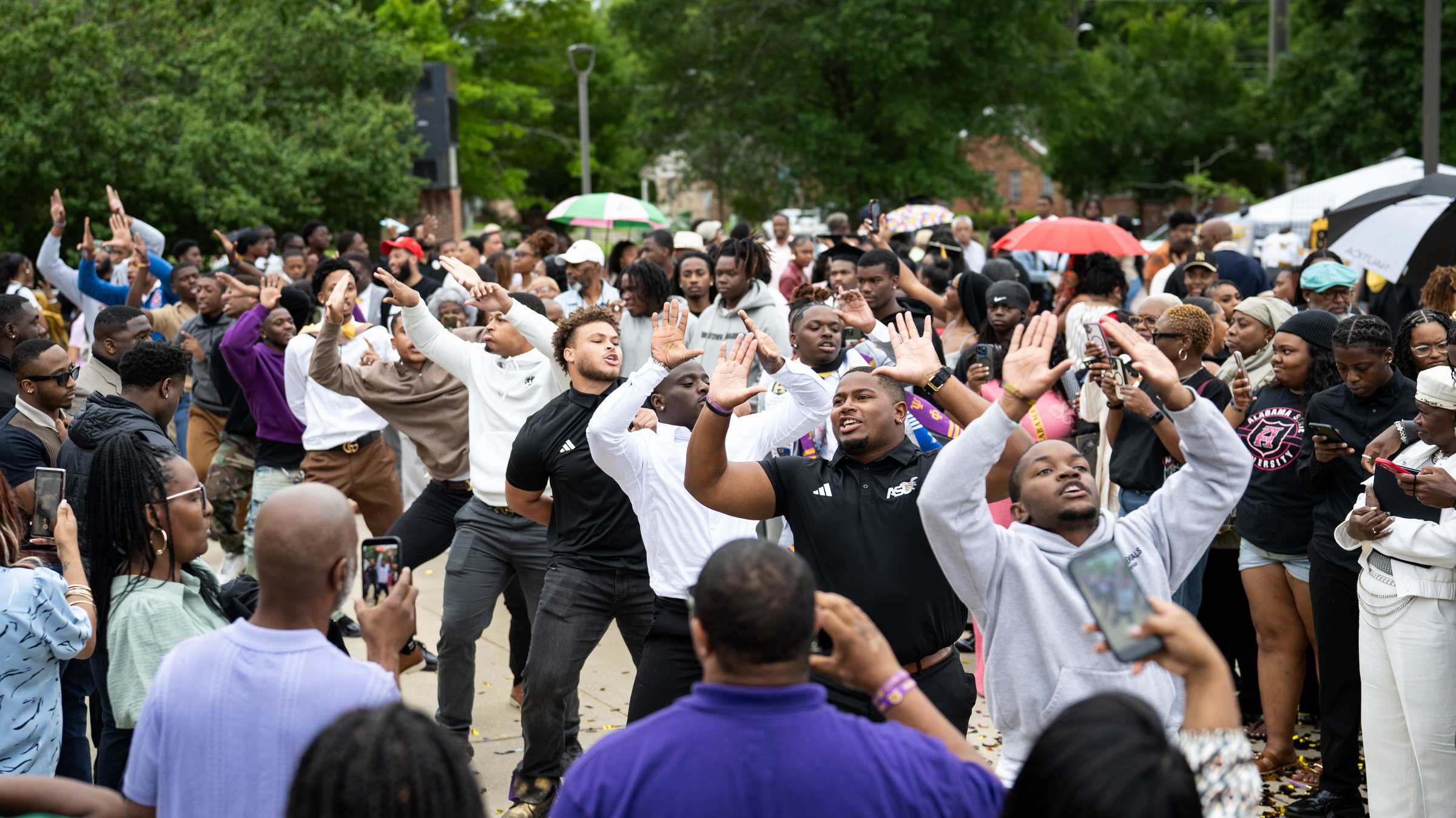 A crowd of Alabama State students celebrates together outdoors, hands raised.